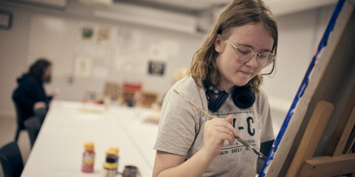 Elev står och målar på en blå tavla